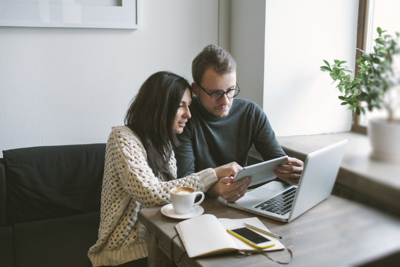 Young couple working in cafe with tablet, laptop, smartphone, notepad and coffee on the table